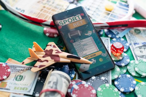 Online gaming betting app on smartphone with casino chips, money, and sports equipment