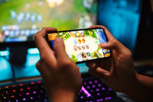 Person playing online gaming on a smartphone, showing a mobile game interface with colorful graphics